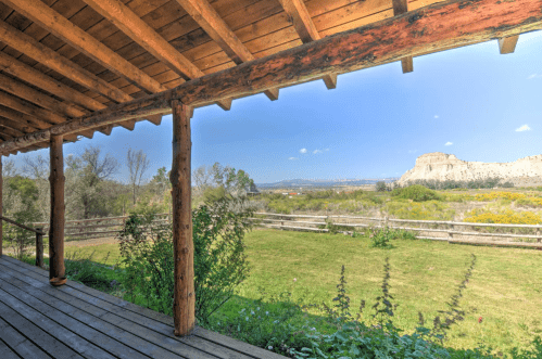 View from a wooden porch overlooking a grassy field and distant cliffs under a clear blue sky.